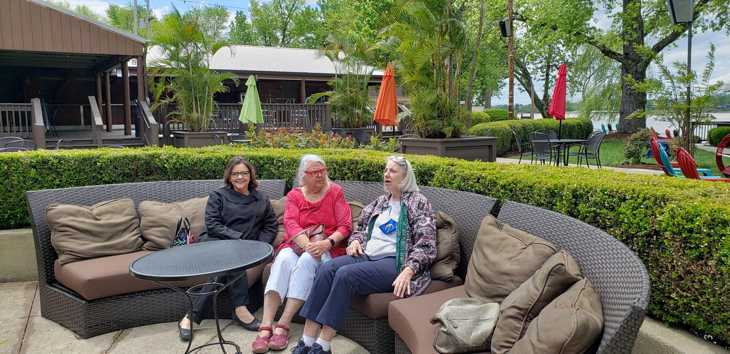 Three women sitting on a couch outside in the sun.