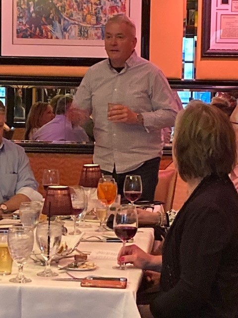 A man standing at the head of a table with wine glasses.