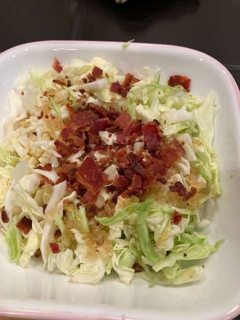 A white bowl of food with bacon and cabbage.