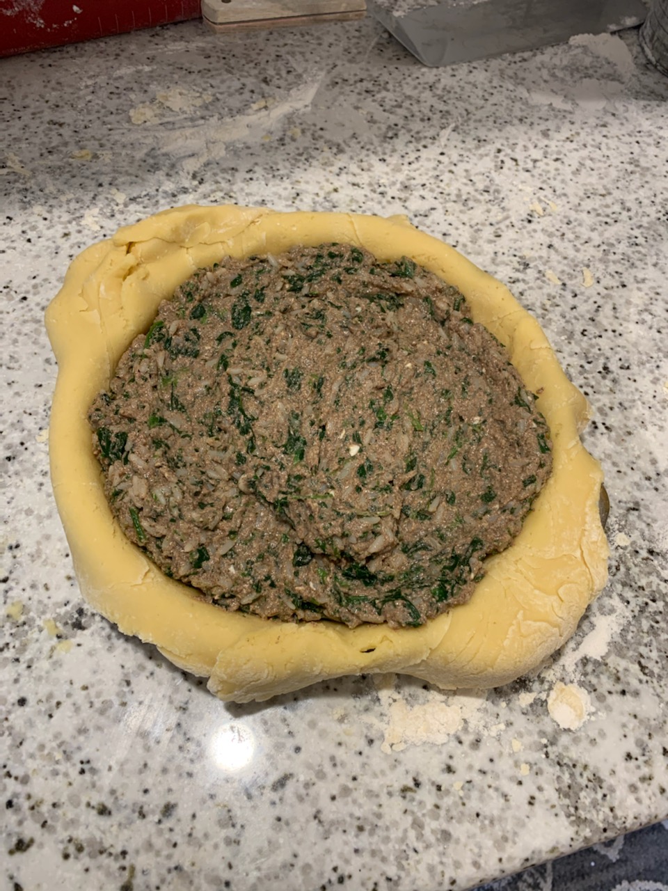 A pie crust with meat and spinach inside of it.