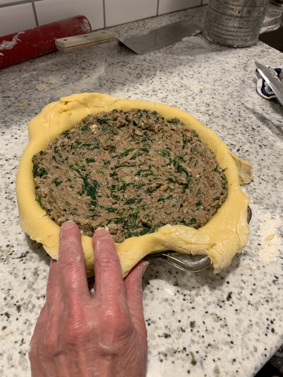 A person holding onto the dough for making meat and vegetable pie.