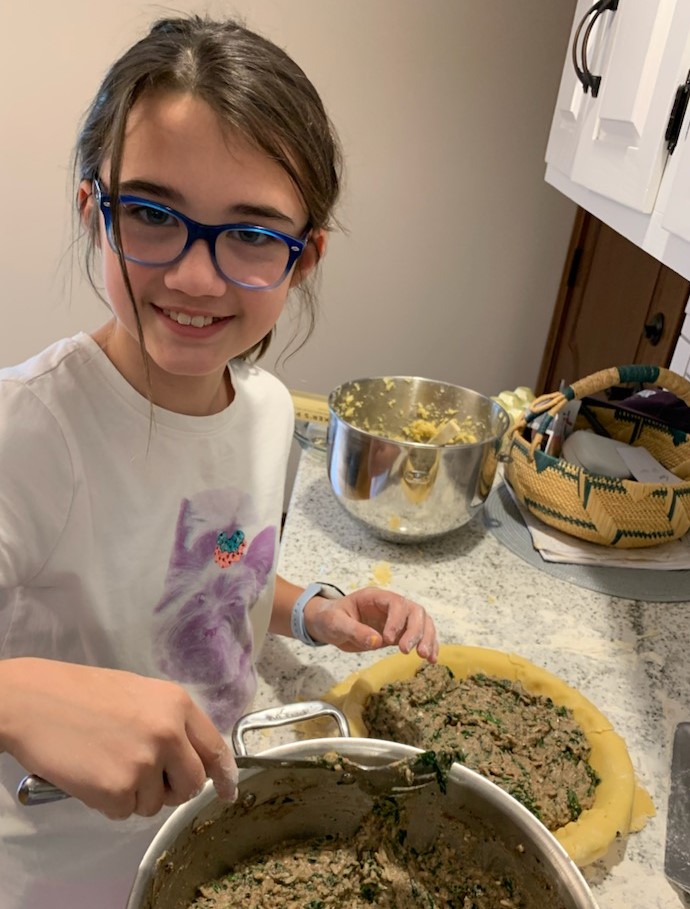 A girl in glasses is cutting food on the counter.