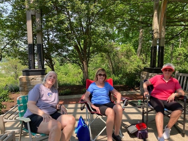 P7 Three women sitting on lawn chairs in front of trees.