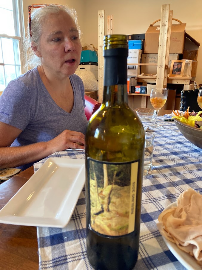 A woman sitting at the table with a bottle of wine.