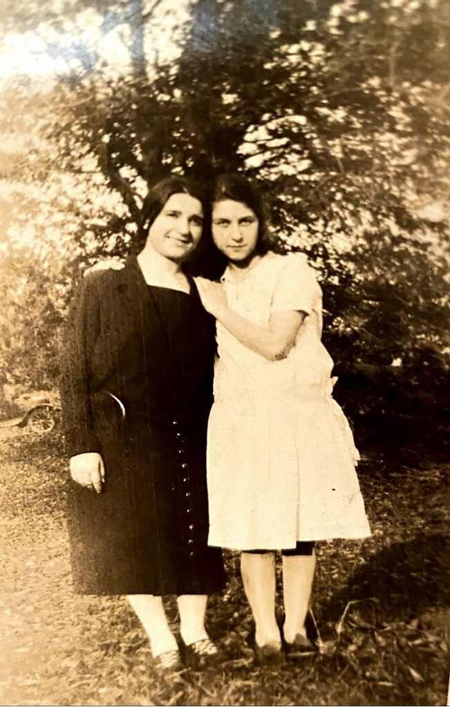 Two women standing next to each other in a park.