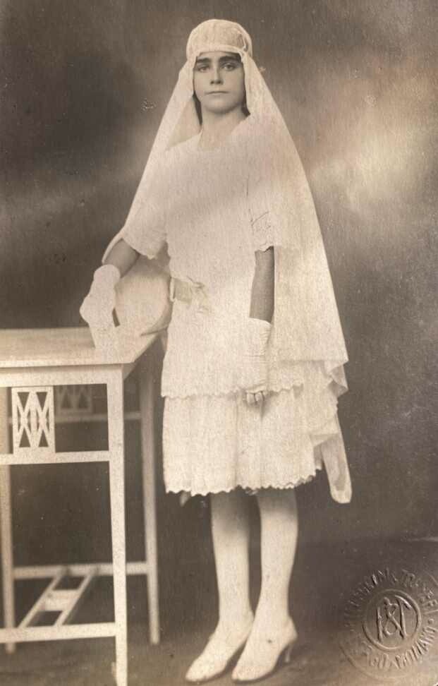 A young girl in white dress holding a tennis racket.