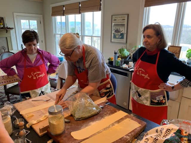 Three women in aprons preparing food on a table.